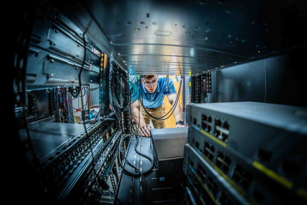A person working inside a server room is meticulously examining equipment and wires, ensuring top-notch information security.
