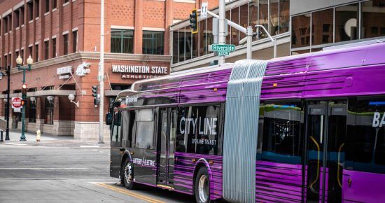 A purple City Line bus on a street corner in front of a red brick building with a Washington State Athletic sign.